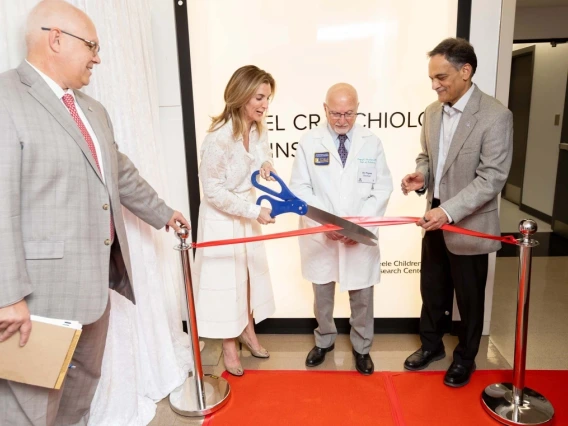 Four people smiling and talking while using large scissors to cut a ribbon