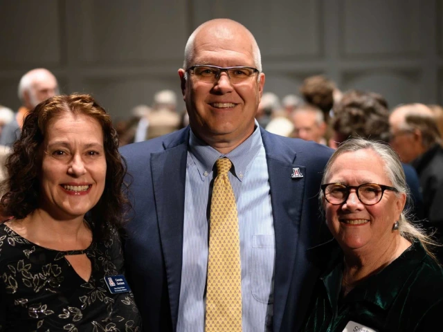 A group of three people smiling with their arms around each other at a reception.