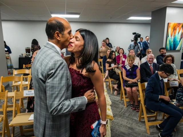 Two people smiling and taking with a vase of flowers in front of them