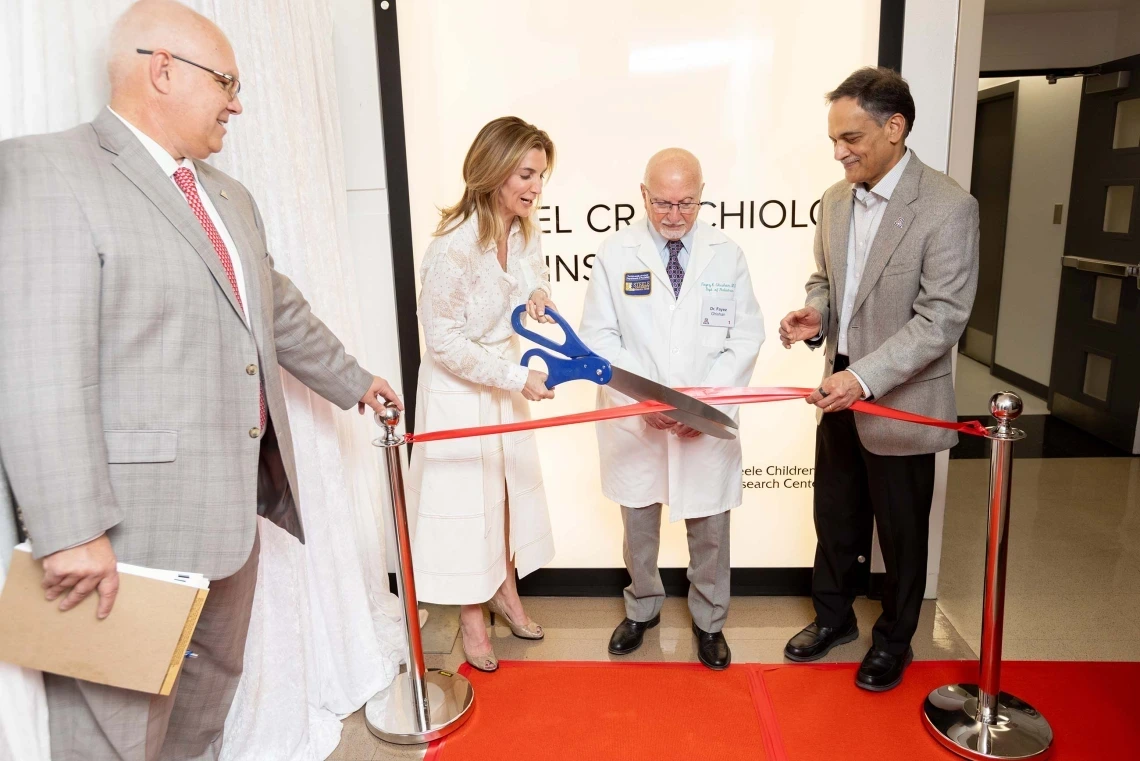Four people smiling and talking while using large scissors to cut a ribbon