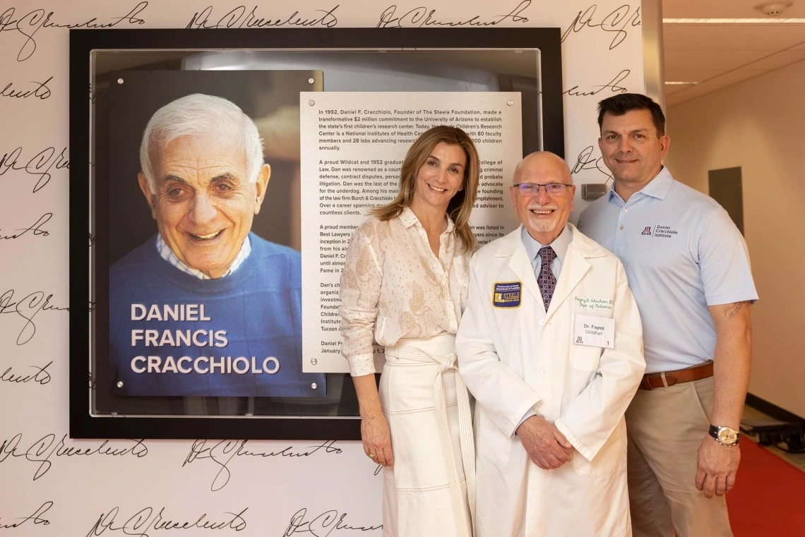 Three people smiling in front of a framed photo of Daniel Francis Cracchiolo 