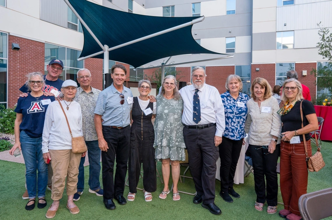 A group of 11 people standing and smiling with their arms around each other at the W.A. Franke Honors College courtyard