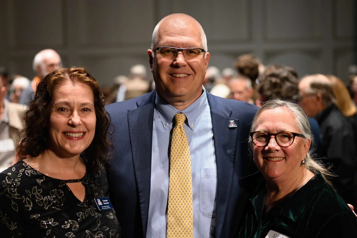 A group of three people smiling with their arms around each other at a reception.