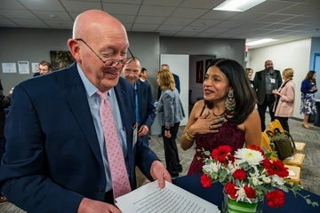 Two people smiling and taking with a vase of flowers in front of them