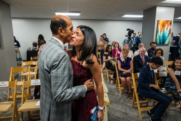 Two people smiling and taking with a vase of flowers in front of them