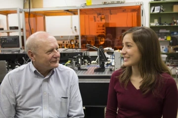 Two people converse in a University of Arizona holography lab, surrounded by optical research equipment.