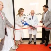 Four people smiling and talking while using large scissors to cut a ribbon