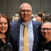 A group of three people smiling with their arms around each other at a reception.