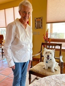 A woman smiling alongside her dog, who is sitting in a chair